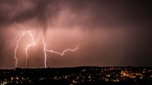 A powerful lightning storm illuminates the night sky over a cityscape, creating a dramatic scene.